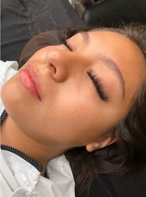 Woman resting on brown pillow with eyes closed, showing eyelash extensions and groomed eyebrows.