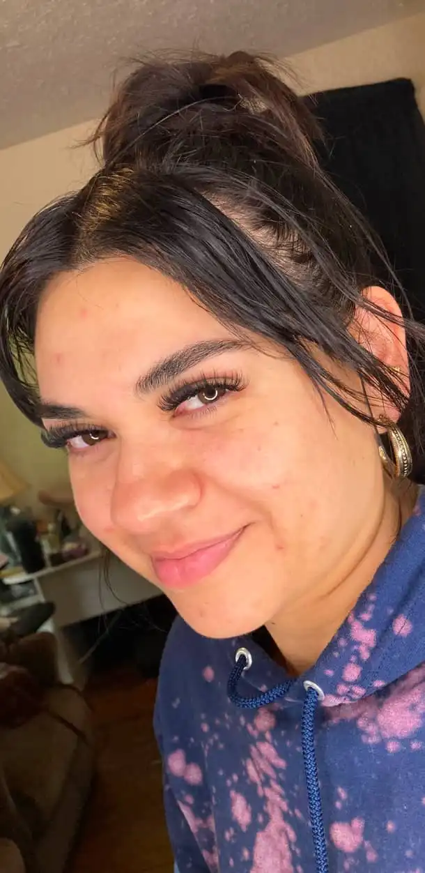 Smiling woman with dark hair and eyelash extensions wearing a blue and pink hoodie