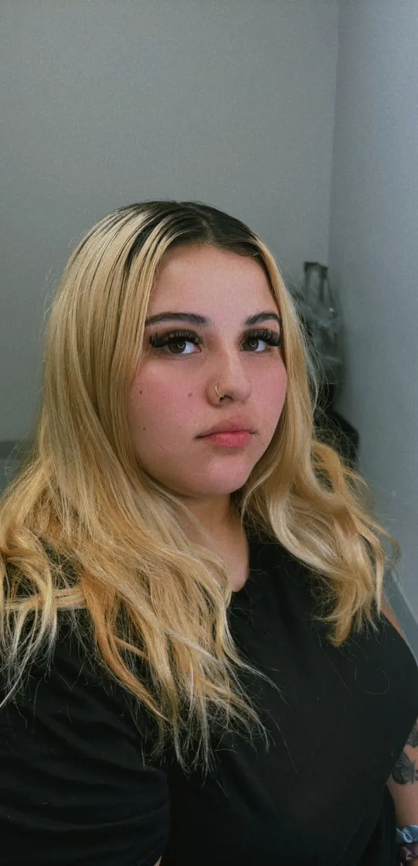 Close-up of young woman with long eyelash extensions, defined eyebrows, and nose piercing.